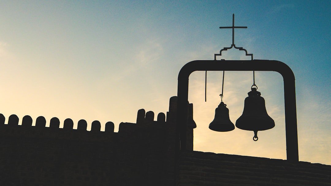 A silhouette of a church with bells hanging from it's roof